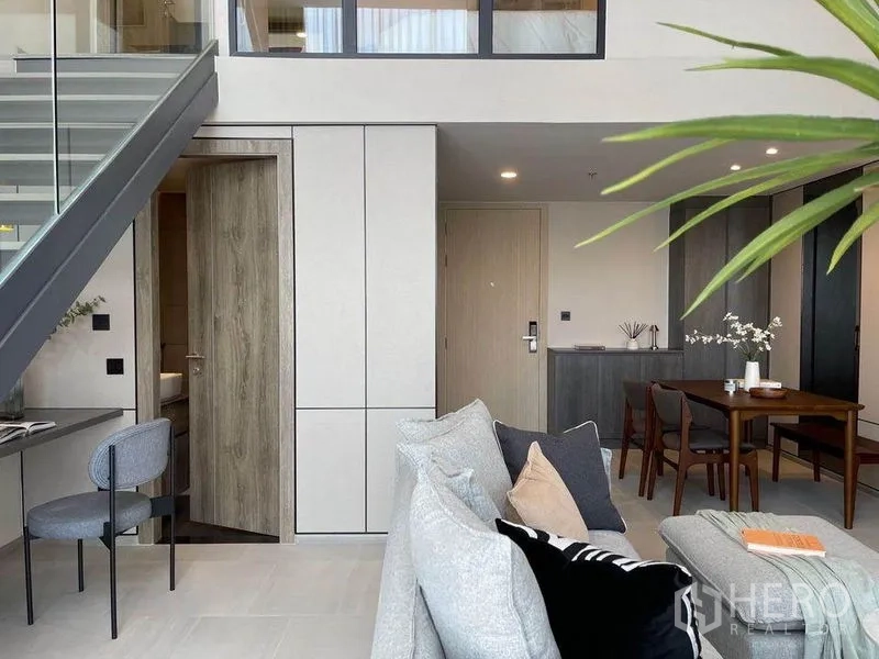 Condominium for rent in Pathum Wan, Bangkok - Light-filled living space with entry door, tall storage cabinets, dining table and a work desk beneath the glass stair.