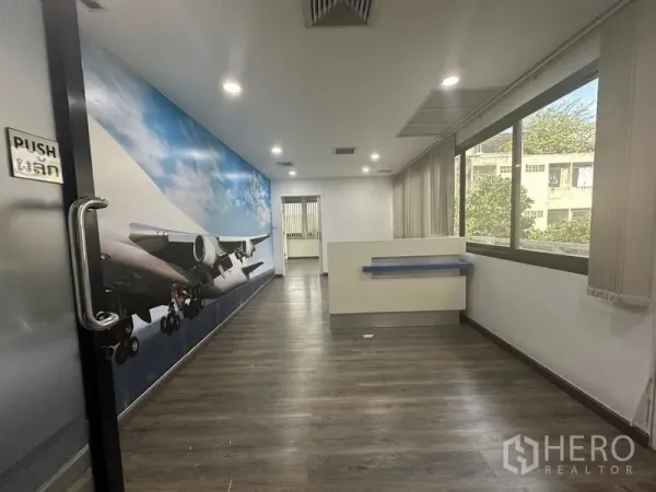 办公空间 出租在Khlong Toei, Bangkok - 明亮的办公室走廊，飞机主题壁画、木纹地板与大窗户