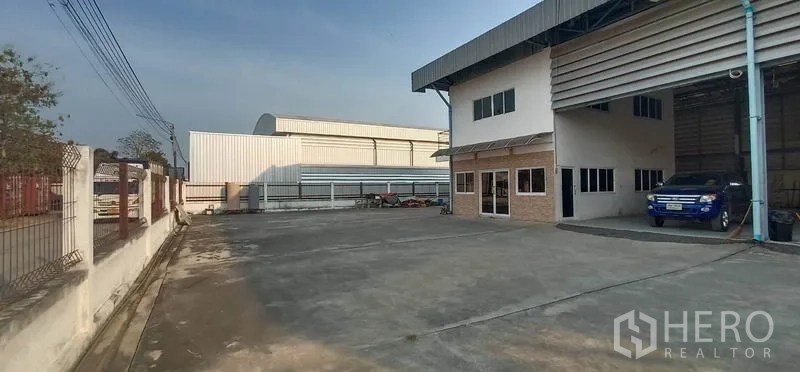 Warehouse for rent in Khlong Luang, Pathum Thani - Spacious concrete yard with an attached two-storey office beside the warehouse loading bays, suitable for truck parking.