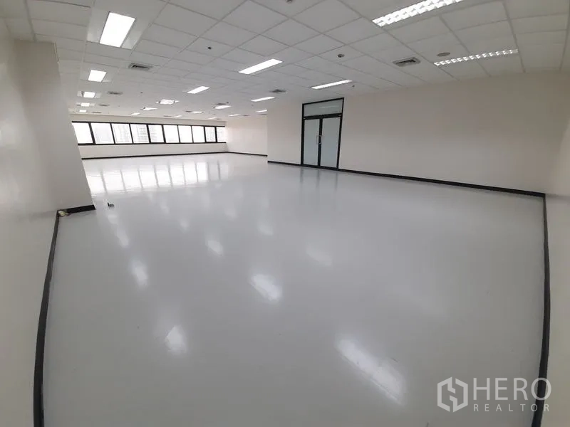 Office Space for rent in Bang Rak, Bangkok - Large open‑plan office with glossy flooring, long window wall, grid ceiling lights and a glass entry door.