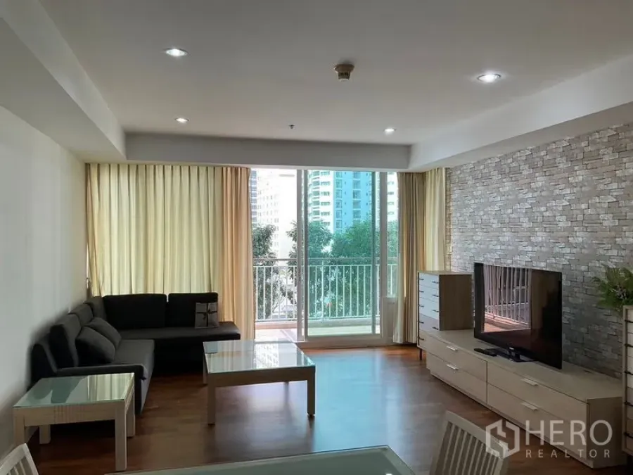 Condominium for rent in Khlong Toei, Bangkok - Bright living room with balcony access, sofa, TV console, and stone accent wall.