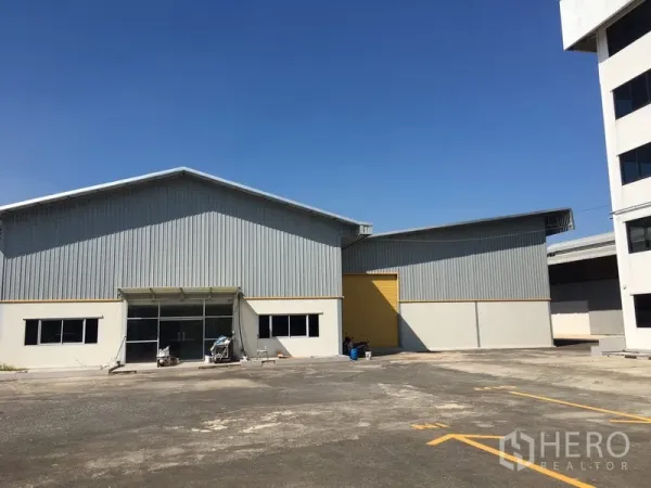 Warehouse for rent in Saphan Sung, Bangkok - Twin metal-clad warehouse buildings with wide driveway and a yellow roller shutter door.