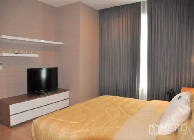 Condominium for rent or sale in Watthana, Bangkok - Bedroom angle showing TV unit, blackout curtains, and wood flooring.