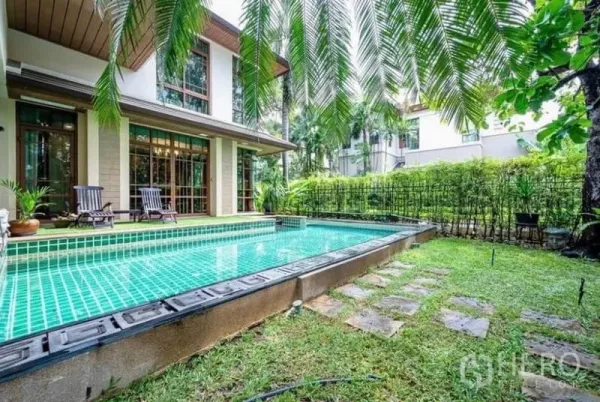 Detached House for rent in Khlong Toei, Bangkok - Private turquoise-tiled swimming pool beside a landscaped garden and deck chairs at the rear of the house.