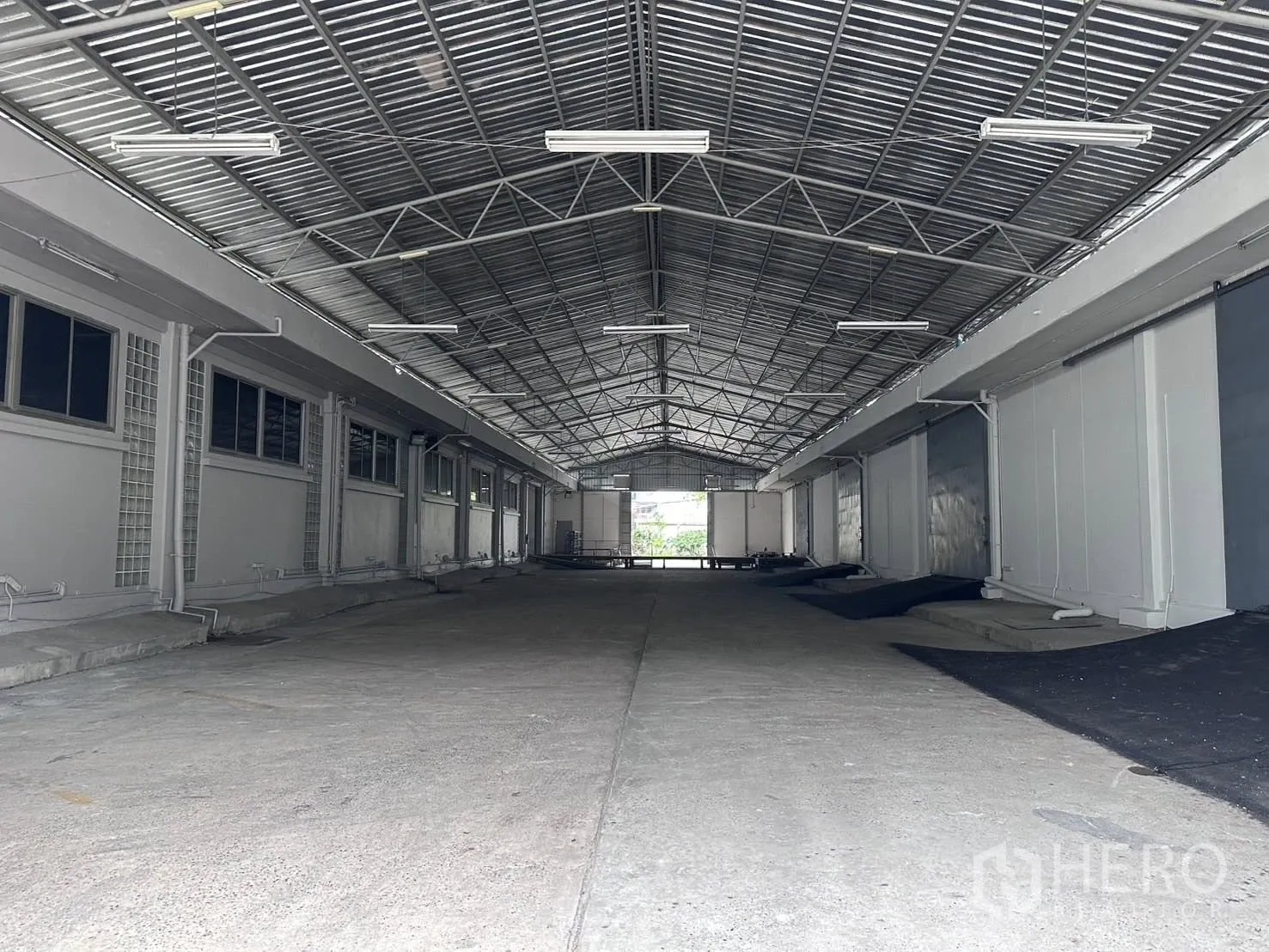 Warehouse for rent in Mueang Samut Prakan, Samut Prakan - Covered loading corridor with steel truss roof and multiple roller shutter bays inside the warehouse.