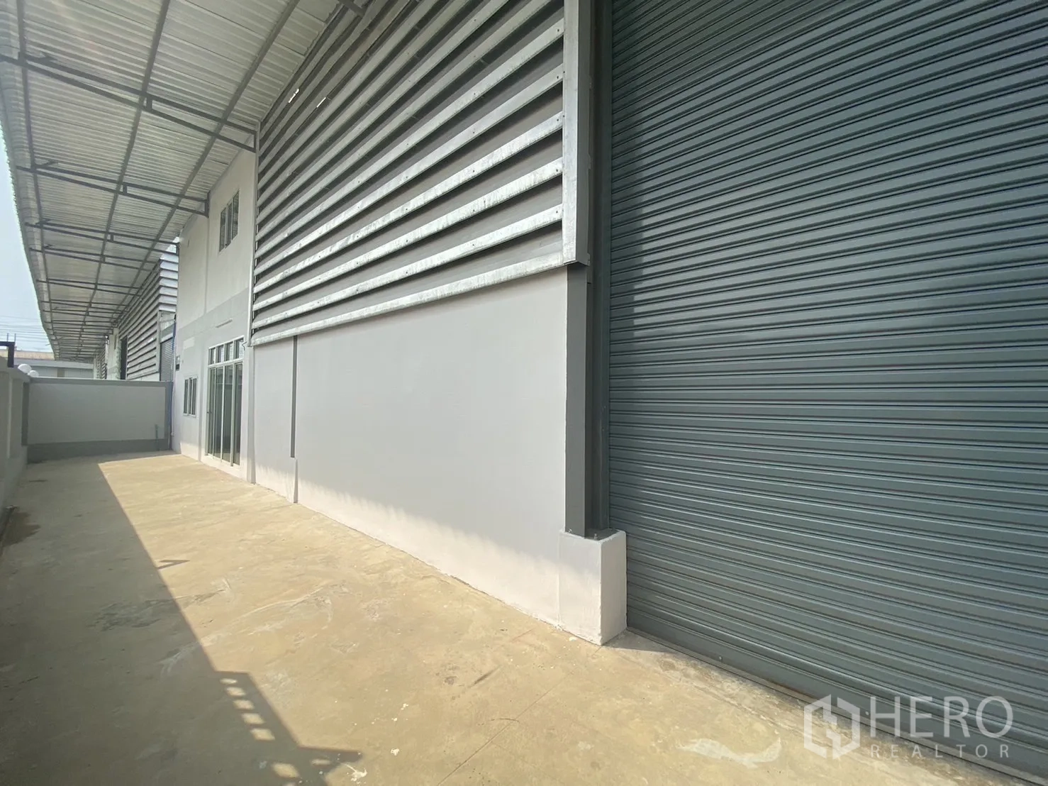 Factory for rent or sale in Mueang Samut Sakhon, Samut Sakhon - Side elevation of the factory with large roller shutter and long concrete yard for loading.