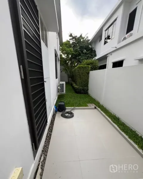 Detached House for rent in Samut Prakan - Service yard with tiled patio, air-conditioning units, and a narrow green strip.