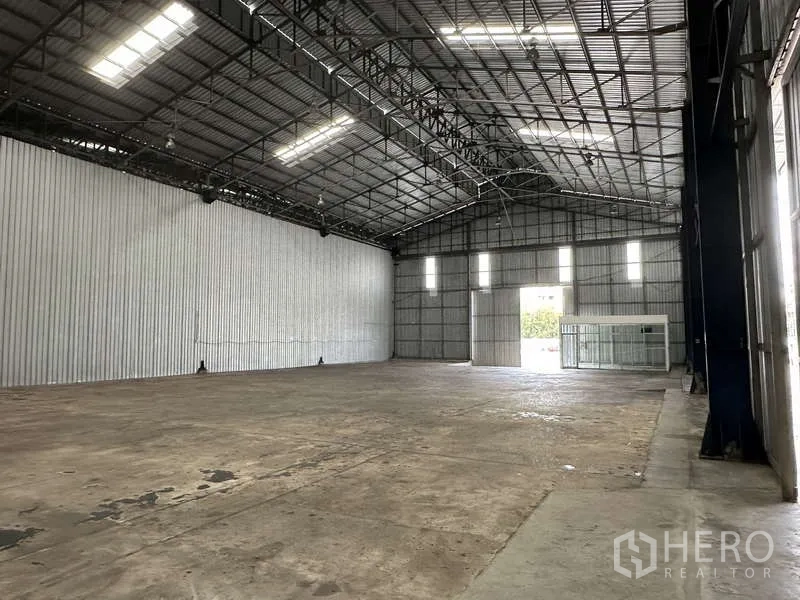 Warehouse for rent in Pak Kret, Nonthaburi - Open storage bay with clerestory windows, wide doorway, and glass office room.