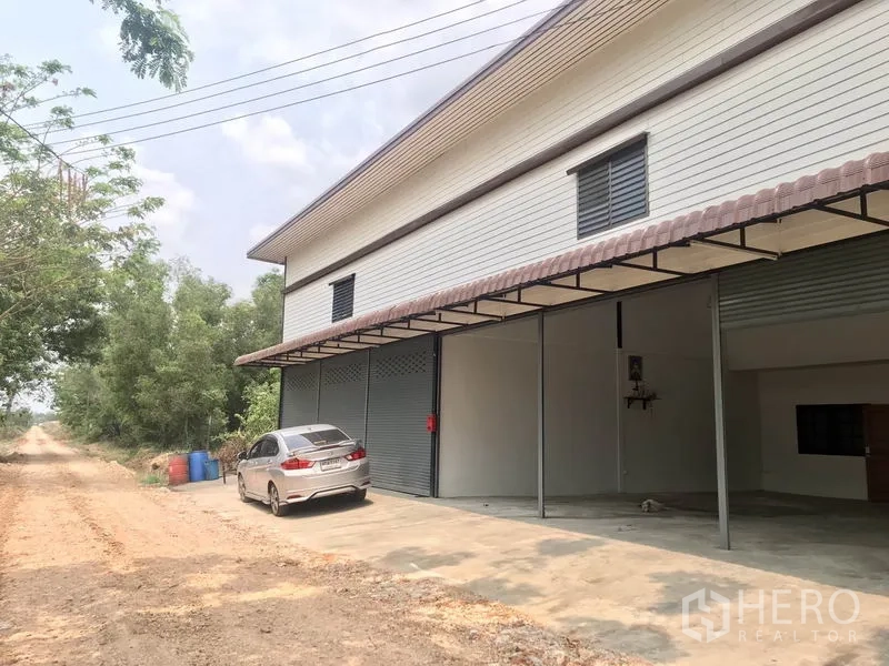 คลังสินค้า ให้เช่าในPathum Thani - ภายนอกมีประตูม้วนหลายบานพร้อมลานคอนกรีตสำหรับจอดรถและขนถ่าย.
