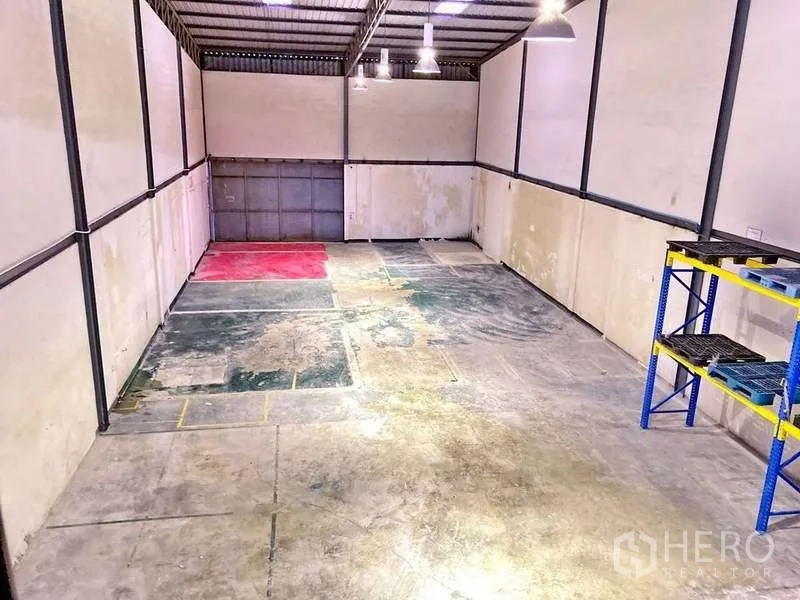 Factory for rent in Samut Prakan - Warehouse interior with high ceiling, pendant lights and concrete floor, showing marked work zones.