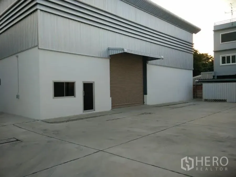 Warehouse for rent in Suan Luang, Bangkok - Warehouse exterior with roller-shutter loading bay, side door and windows on a large paved yard.
