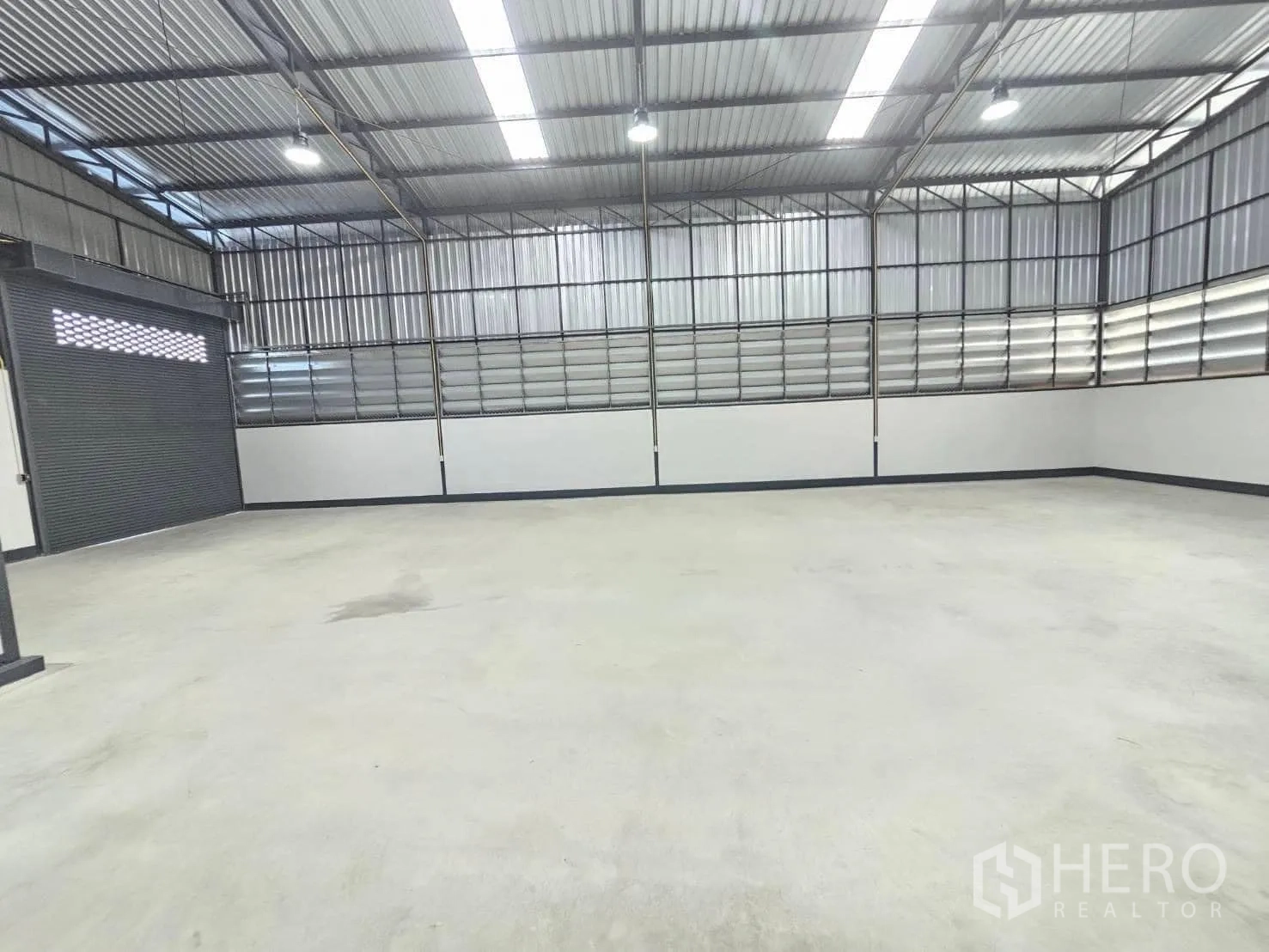 Warehouse for rent in Lam Luk Ka, Pathum Thani - Interior corner showing a roller shutter door and a wall-mounted electrical panel.