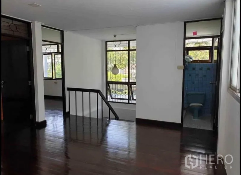 Detached House for rent in Lat Phrao, Bangkok - Second‑floor landing with wood flooring, stair rail and doorway to a blue‑tiled bathroom.