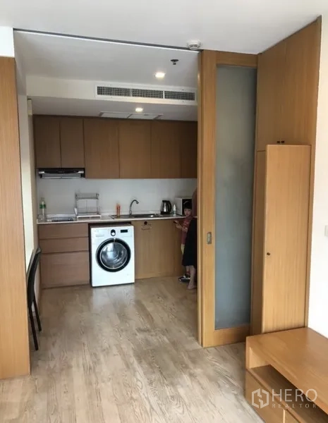 Condominium for rent in Khlong Toei, Bangkok - Kitchen separated by sliding glass partition with washer, upper cabinets and counter space.