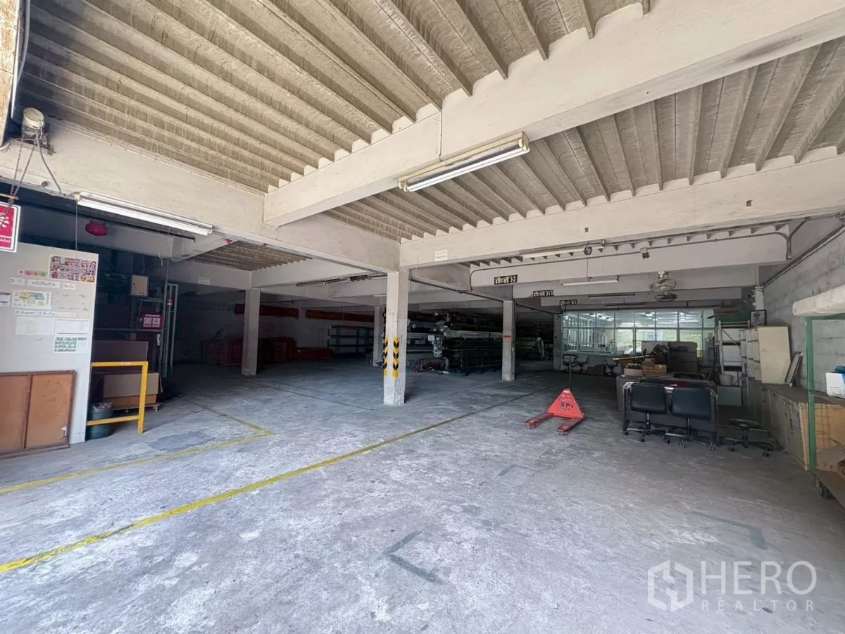 Factory for rent or sale in Bang Khun Thian, Bangkok - Open storage and packing area with pallet jack and adjacent office corner.