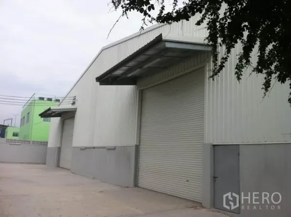 Warehouse for rent in Sai Mai, Bangkok - Exterior of corrugated metal warehouse with multiple roller doors, covered loading canopies and wide paved yard for truck access.