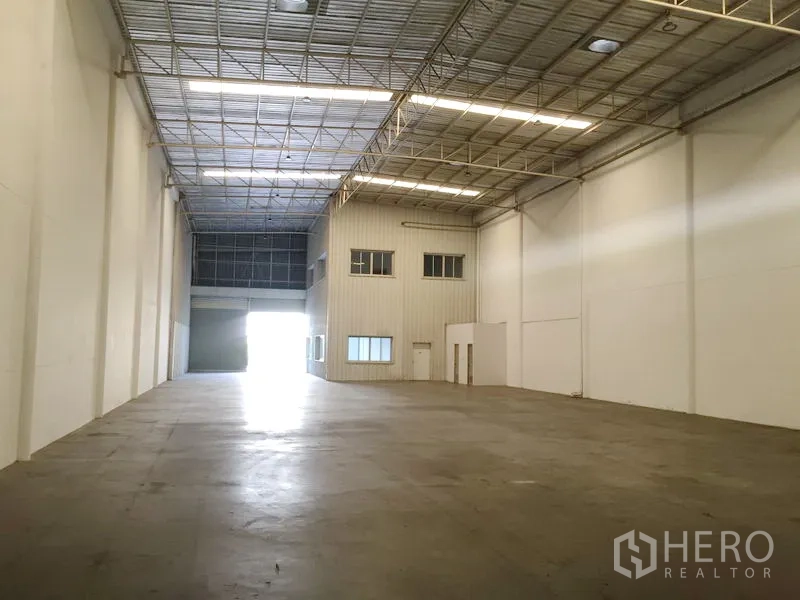 Factory for rent in Khlong Luang, Pathum Thani - Spacious empty factory hall with an attached two-story office pod, roller door entry, and polished concrete floor.