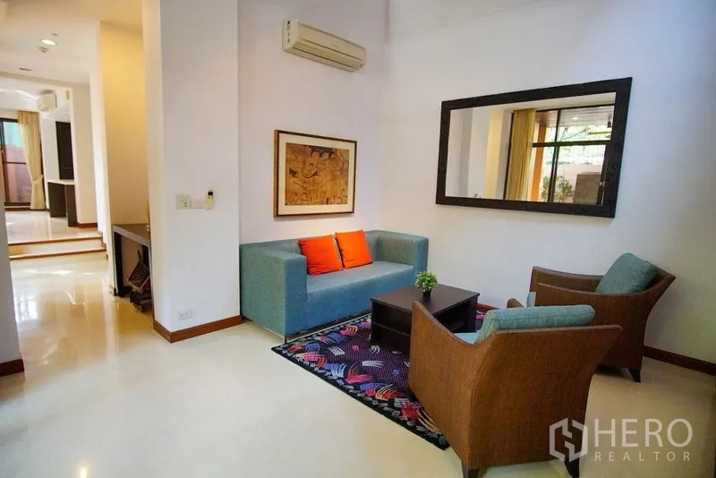 Townhouse for rent in Watthana, Bangkok - Cozy sitting room featuring a teal sofa, rattan armchairs, and a colorful rug.