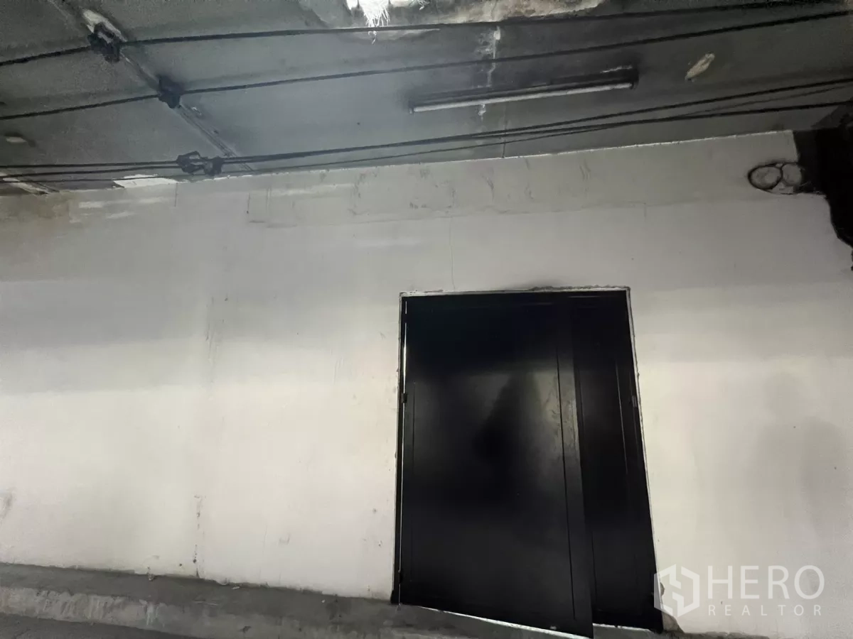 Shophouse for sale in Suan Luang, Bangkok - Close-up of black metal double door under a flyover with service cables.