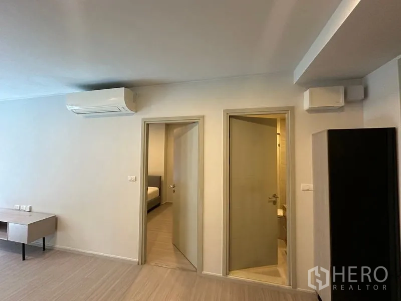 Condominium for rent in Khlong Toei, Bangkok - Hallway showing doors to bedroom and bathroom with light wood flooring and air conditioning unit.