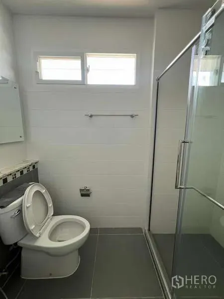 Detached House for rent in Bang Kapi, Bangkok - Compact bathroom with glass shower enclosure, small windows and gray floor tiles.