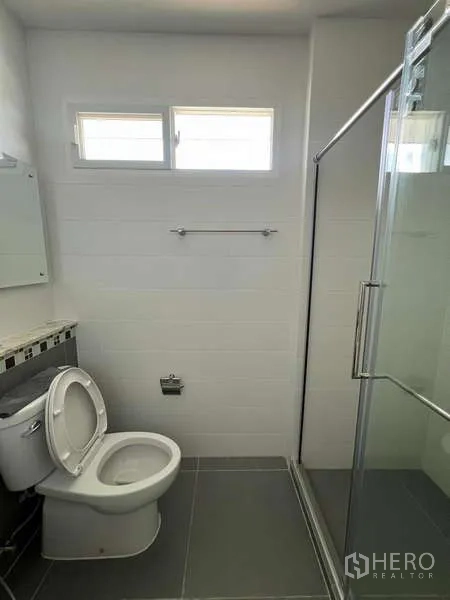 Detached House for rent in Bang Kapi, Bangkok - Compact bathroom with glass shower enclosure, small windows and gray floor tiles.