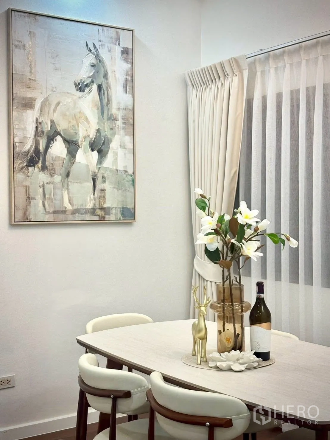 Townhouse for rent in Huai Khwang, Bangkok - Dining corner with light wood table, four chairs, horse artwork, and sheer curtains.