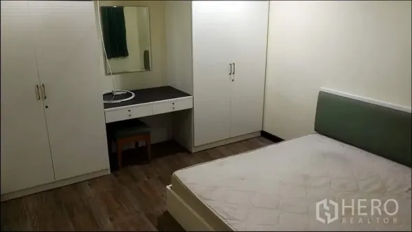Condominium for rent or sale in Khlong Toei, Bangkok - Second bedroom featuring fitted wardrobes, a dressing table, wood flooring, and a queen bed frame.