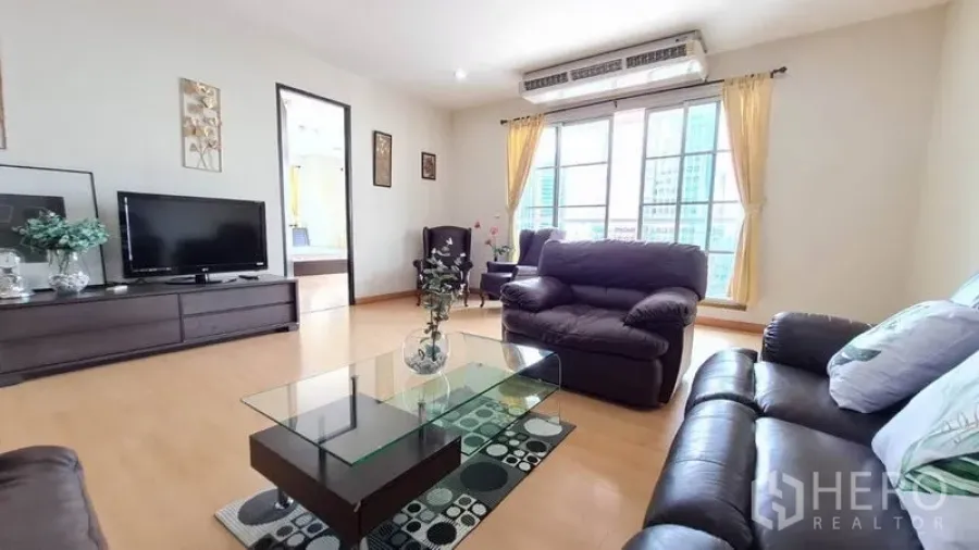 Condominium for rent in Khlong Toei, Bangkok - Bright living room with leather sofas, glass coffee table, TV console and large windows overlooking the Sukhumvit skyline.