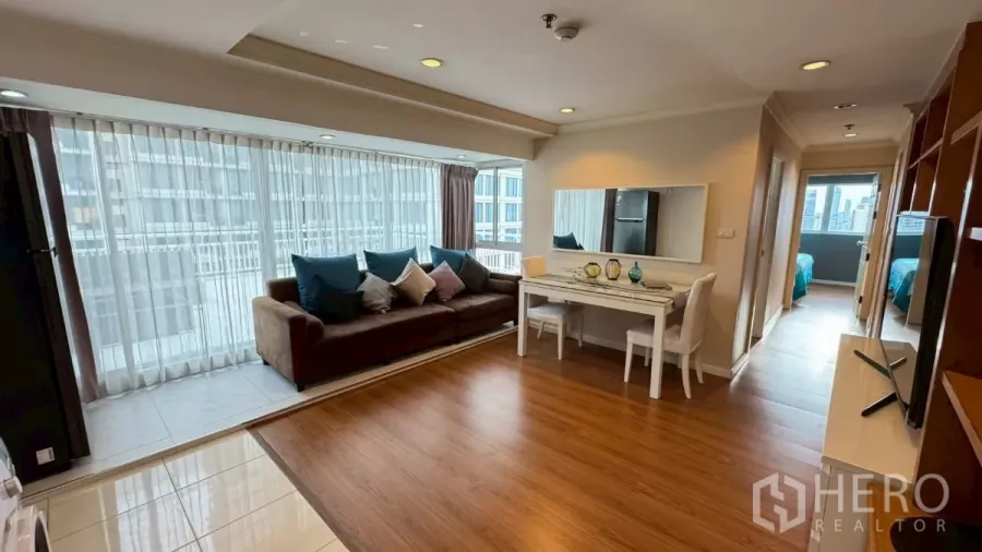 Condominium for rent in Watthana, Bangkok - Sunlit living room with sofa, dining table and wraparound windows.