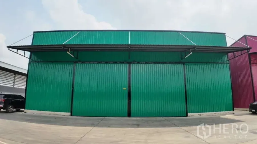 Warehouse for rent in Mueang Chachoengsao, Chachoengsao - Front view of a green metal-clad warehouse with wide sliding doors and a concrete driveway.