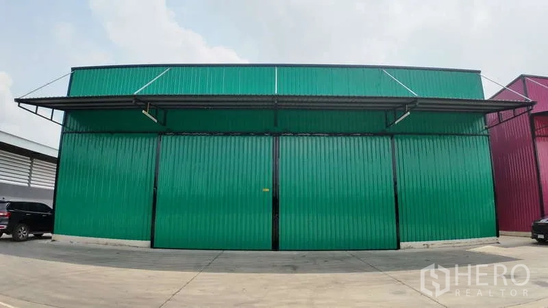 Warehouse for rent in Mueang Chachoengsao, Chachoengsao - Front view of a green metal-clad warehouse with wide sliding doors and a concrete driveway.