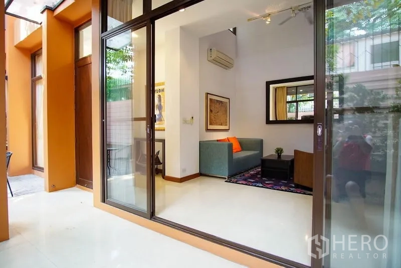 Townhouse for rent in Watthana, Bangkok - Sliding glass doors opening to a bright living area with sofa and wall mirror.
