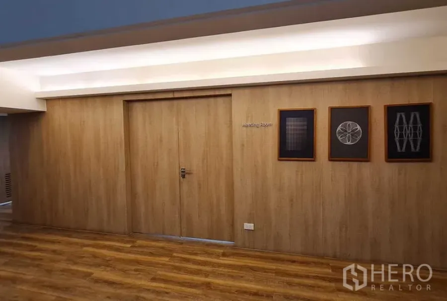 Office Space for rent in Watthana, Bangkok - Wood-clad corridor with double doors to a meeting room, framed artwork and warm recessed lighting over timber flooring.