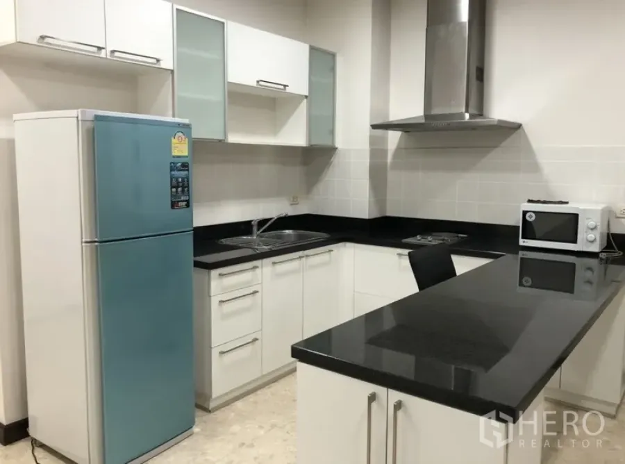 Condominium for rent in Khlong Toei, Bangkok - L-shaped kitchen with black granite countertops, stainless hood, island, and a blue two-door fridge.