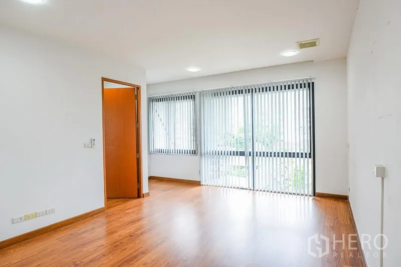 Townhouse for rent in Watthana, Bangkok - Spacious bedroom with large windows and balcony access fitted with vertical blinds.