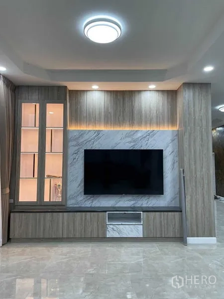 Warehouse for rent or sale in Pathum Thani - Contemporary living room feature wall with mounted TV in wood and marble finishes.
