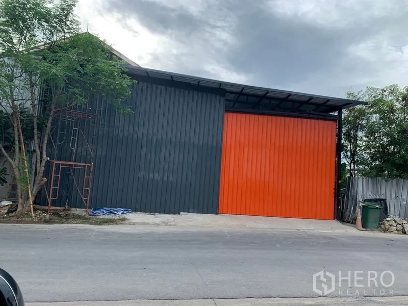 Warehouse for rent in Bang Kapi, Bangkok - Street view of warehouse facade with large orange sliding door and charcoal panels.