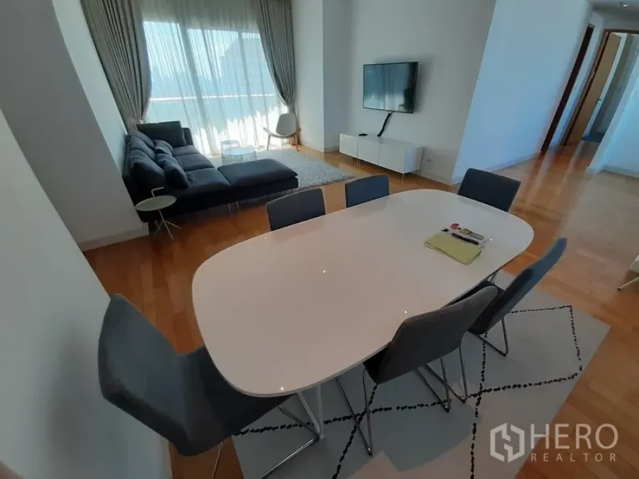 Condominium for rent in Khlong Toei, Bangkok - Six-seat dining table beside the living area with sheer drapes and balcony light.
