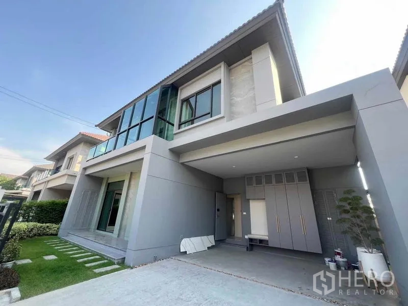 Detached House for sale in Bang Kruai, Nonthaburi - Angled view of the contemporary grey facade showing wide driveway, covered carport and upper-floor corner windows.