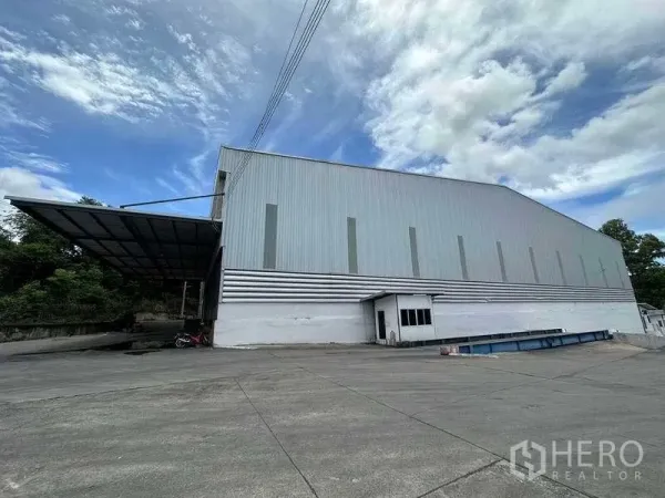 Warehouse for rent in Si Racha, Chon Buri - Side elevation of metal-clad warehouse with loading platform and ample driveway.