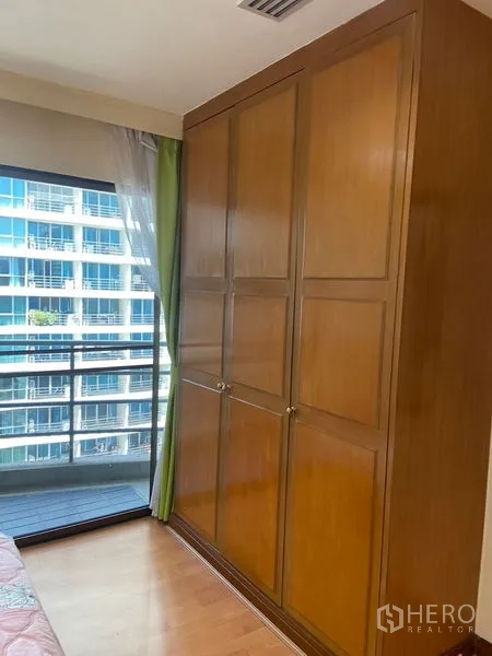 Condominium for rent in Pathum Wan, Bangkok - Built-in wooden wardrobe beside a floor-to-ceiling window with city views.