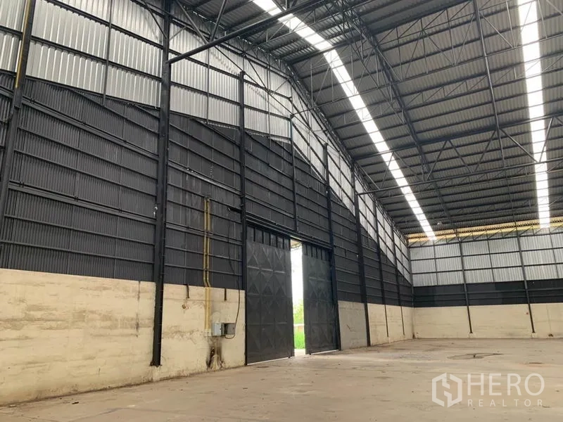 Factory for rent in Chon Buri - Interior of the factory showing tall sliding metal doors, high gabled roof and steel trusses with daylight strips.