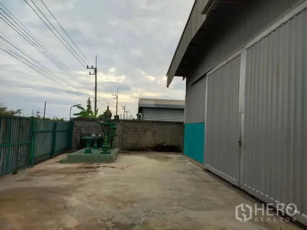 Warehouse for sale in Lam Luk Ka, Pathum Thani - Concrete yard beside the warehouse with sliding gate and a Thai spirit house.