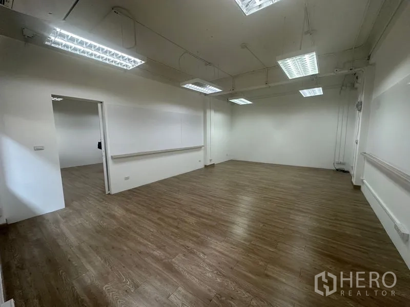 Office Space for rent in Chatuchak, Bangkok - Spacious corner office with suspended fluorescent lights, cable trunking and a sliding door to an adjacent room.