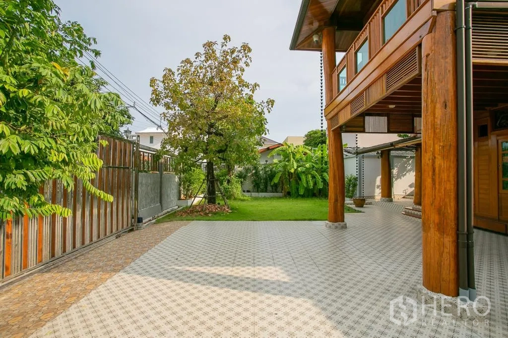 Detached House for rent or sale in Huai Khwang, Bangkok - Wide tiled driveway and covered veranda beside the wooden house facing the lawn.