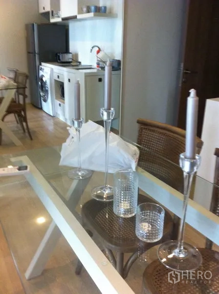 Condominium for rent in Bangkok - Glass dining table set with candles beside a compact kitchen and full-size fridge.