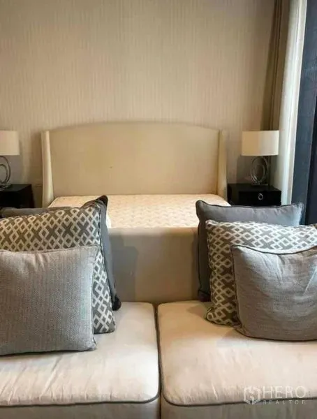 Condominium for rent in Pathum Wan, Bangkok - Cozy bedroom with upholstered headboard, bedside lamps, and a sofa with patterned cushions.