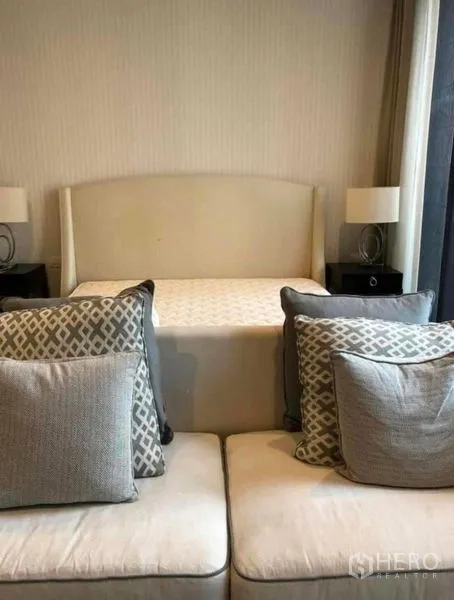 Condominium for rent in Pathum Wan, Bangkok - Cozy bedroom with upholstered headboard, bedside lamps, and a sofa with patterned cushions.