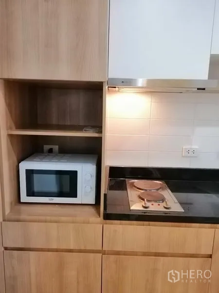 Condominium for rent in Watthana, Bangkok - Kitchen detail showing microwave, cooktop and hood set in wood cabinetry